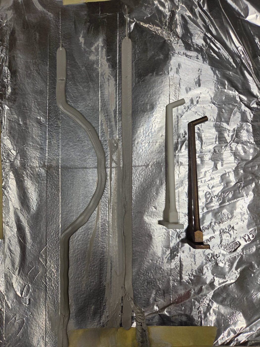 Plastic prototype nozzle and metal printed nozzle lying on foil next to test beads, with handwritten notes
